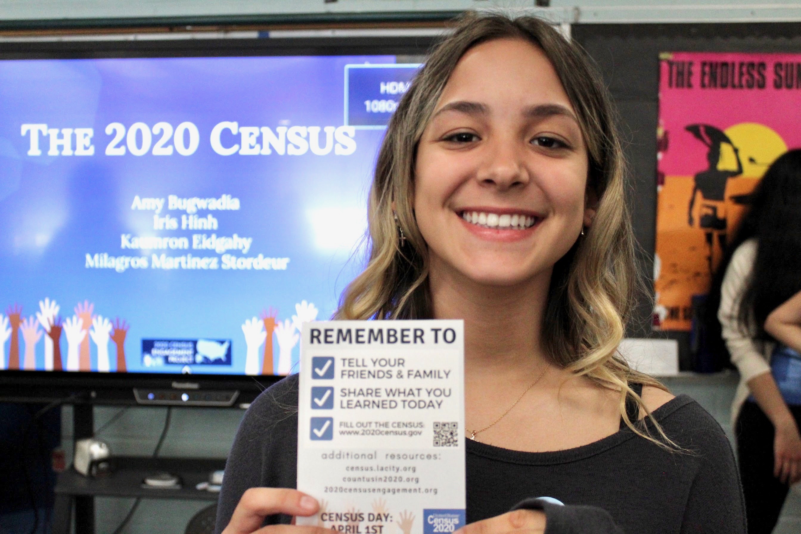 Woman holding a blue sticker that reads I pledged to fill out the 2020 Census