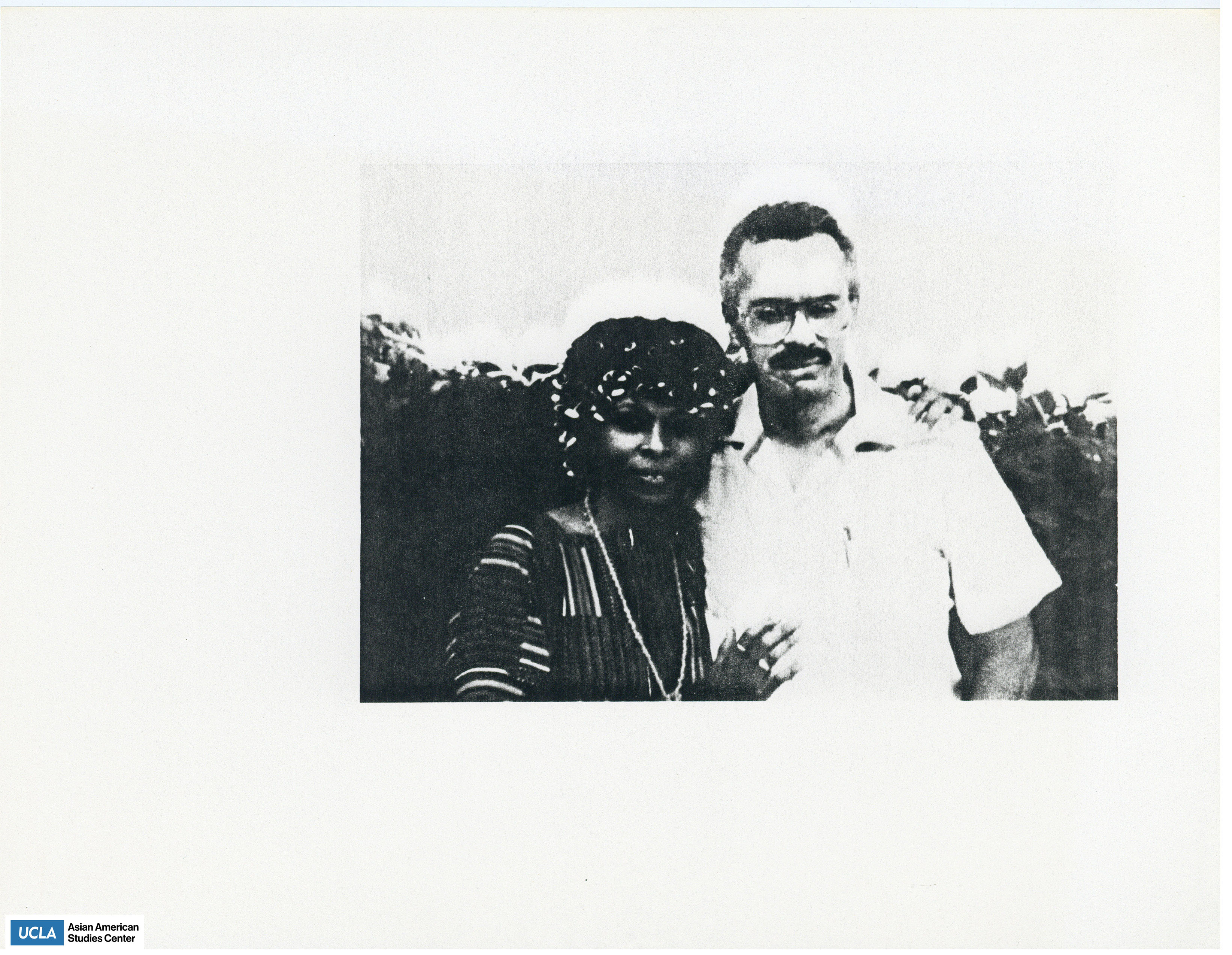 Black and white photograph of a couple. Woman is wearing blouse and man is wearing a short sleeved button shirt.