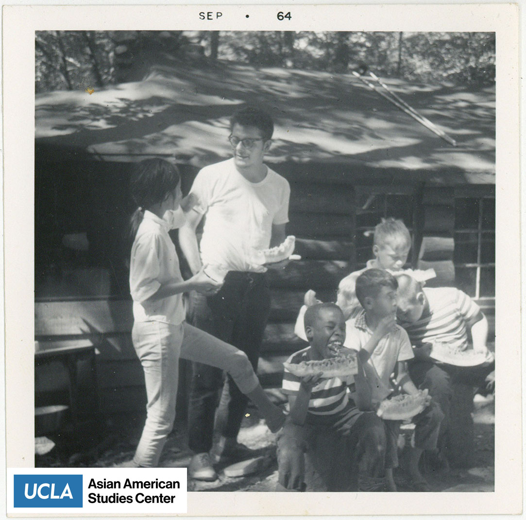 Black and white photograph of what appears to be a summer camp with children eating a slice of watermelon.