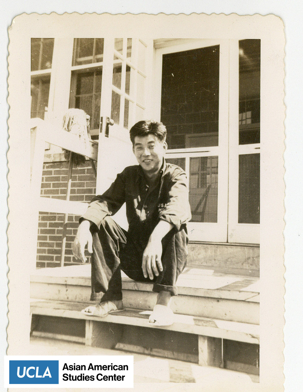 Pete Nakahara, taken at the Rohwer detention facility in McGehee, Arkansas. He is seated on the top steps of a barrack doorway.