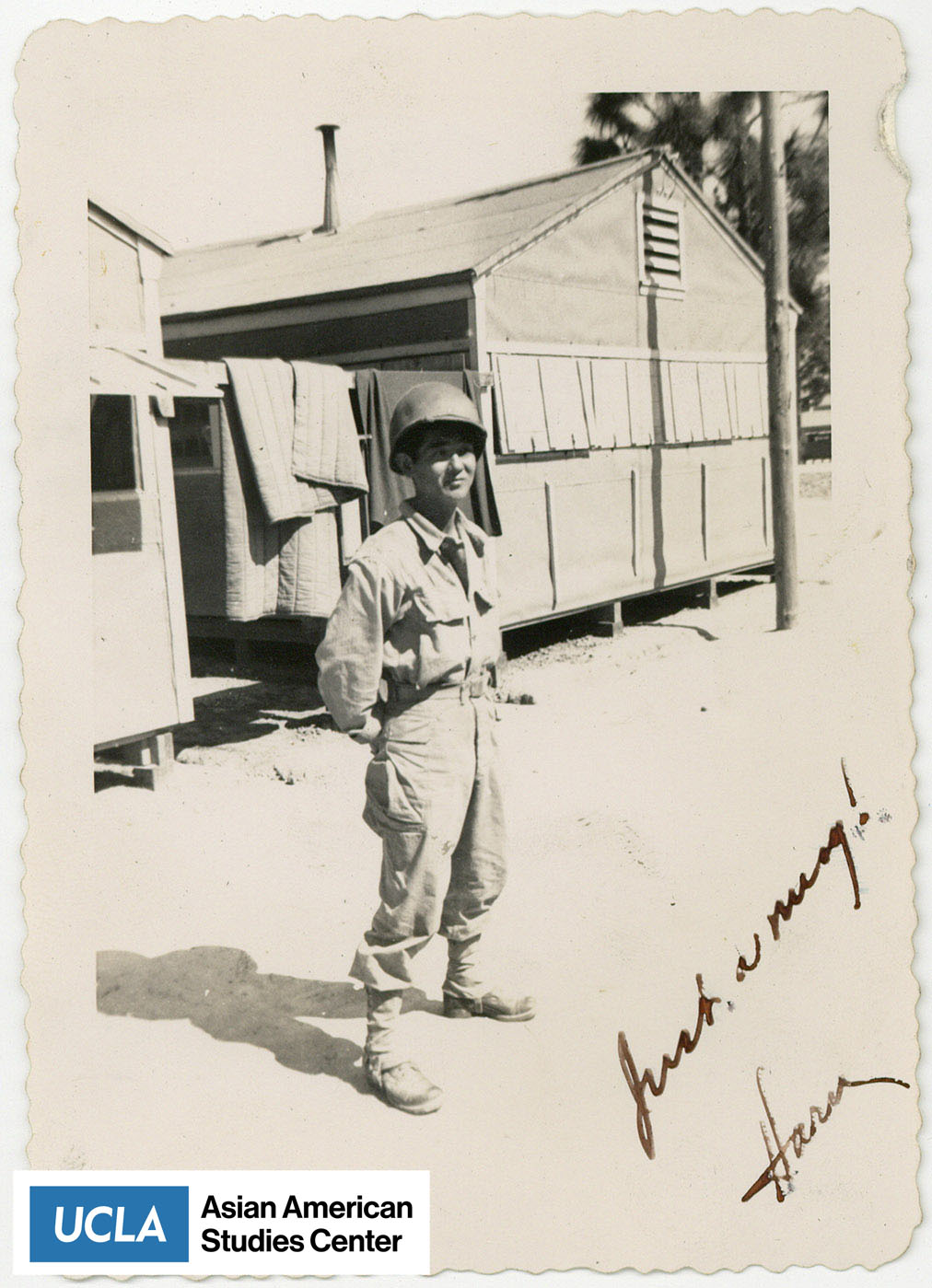 Nisei solider stands next to barracks.