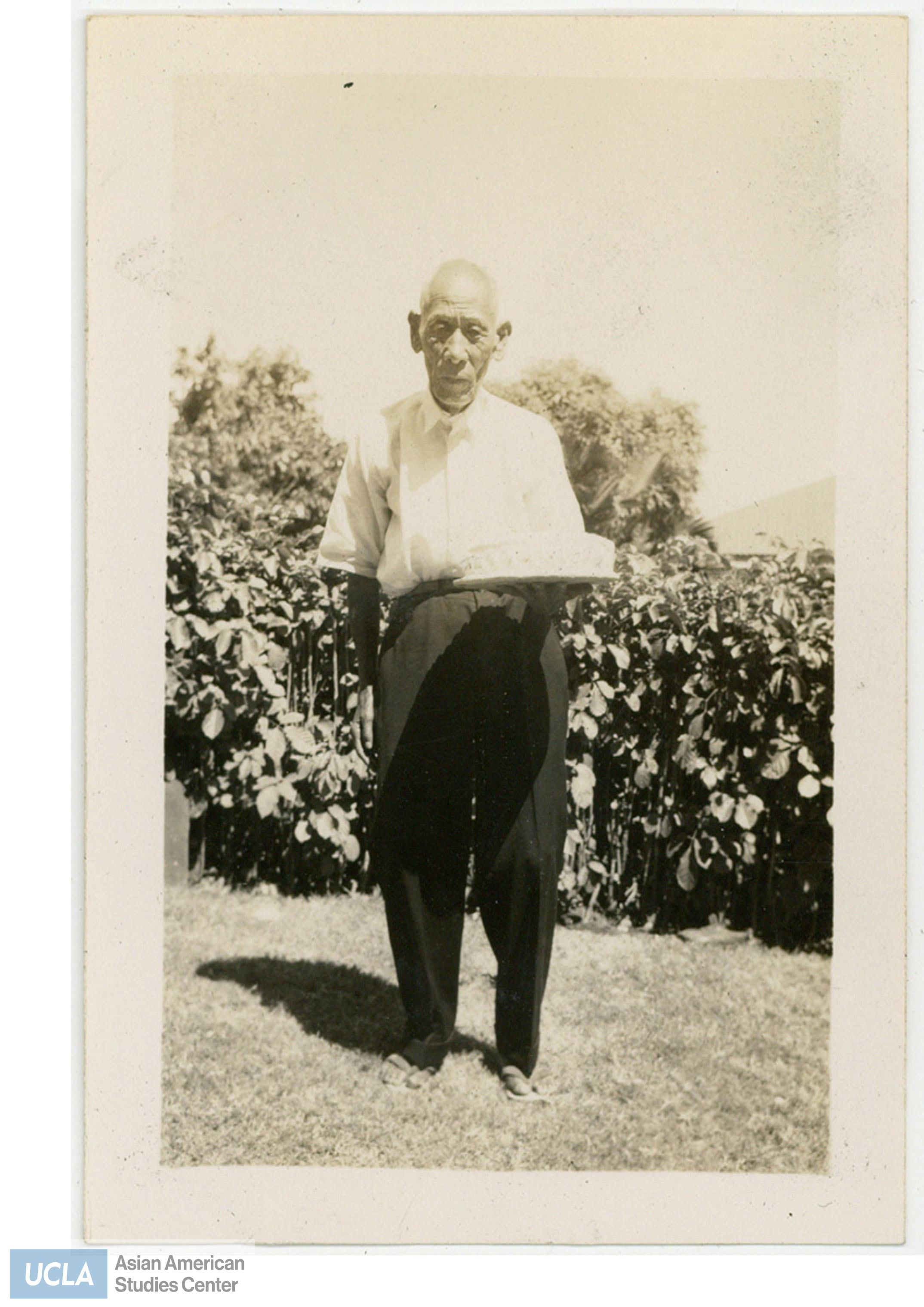 Older Japanese man holding a cake. Back of photo includes text: 