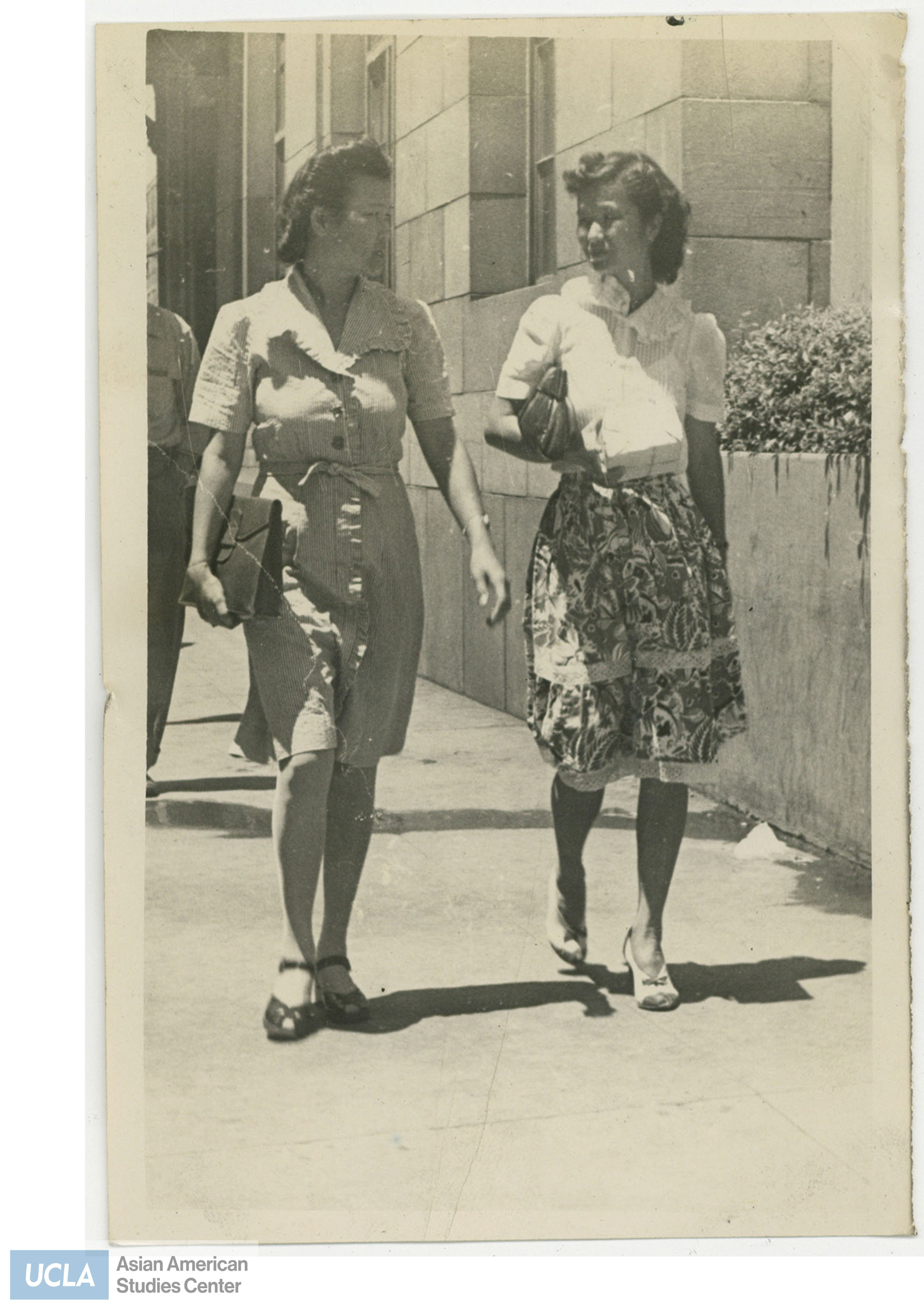 Mrs. Saito and a woman walking on the sidewalk. Back of photo includes text: 