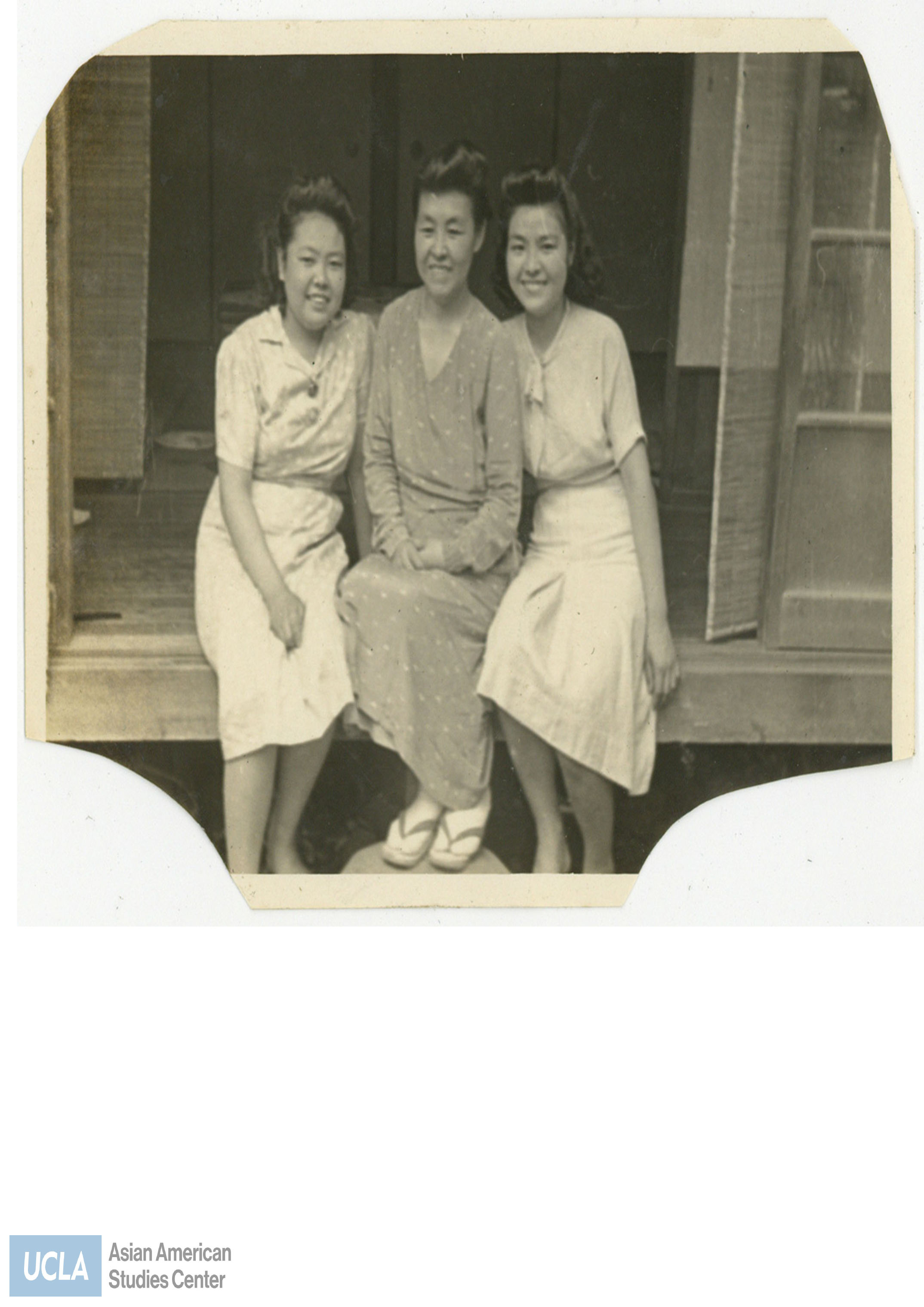 Three women seated together on a sliding door threshold.