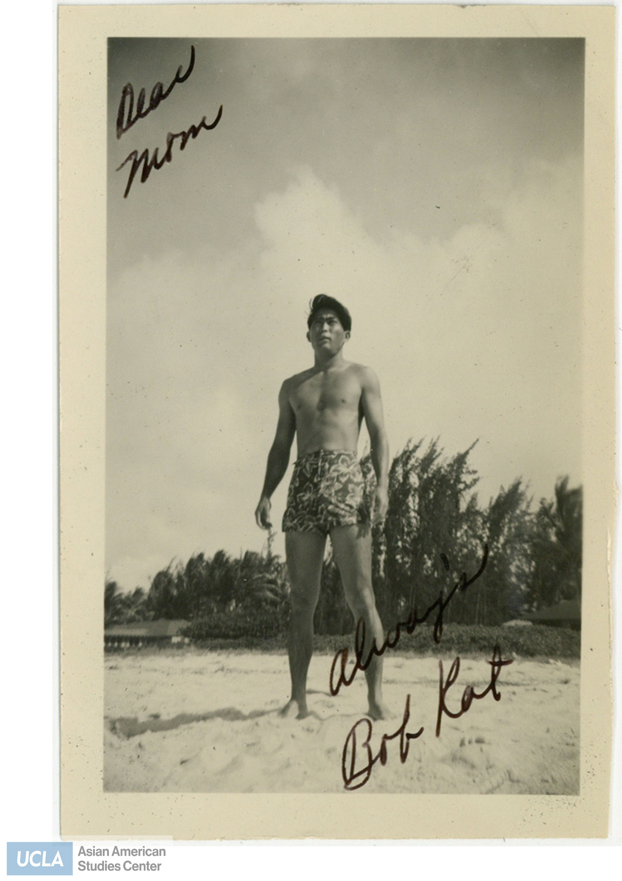 Nisei man standing in the sand of a beach. Back of photo includes text: 