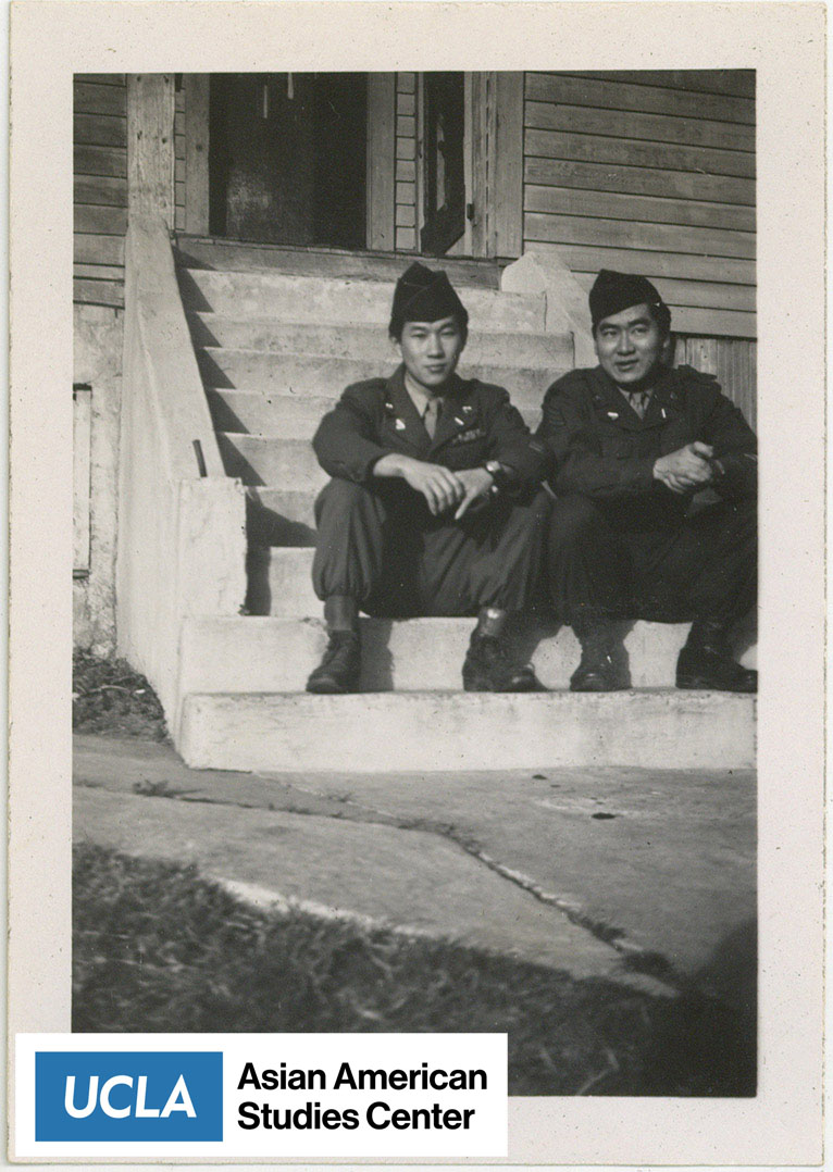 Two Nisei serviceman sit on the steps of stairs.