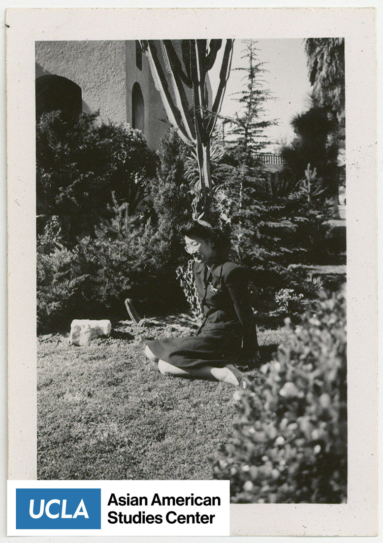 Yuri seated on the grass, surrounded by trees.