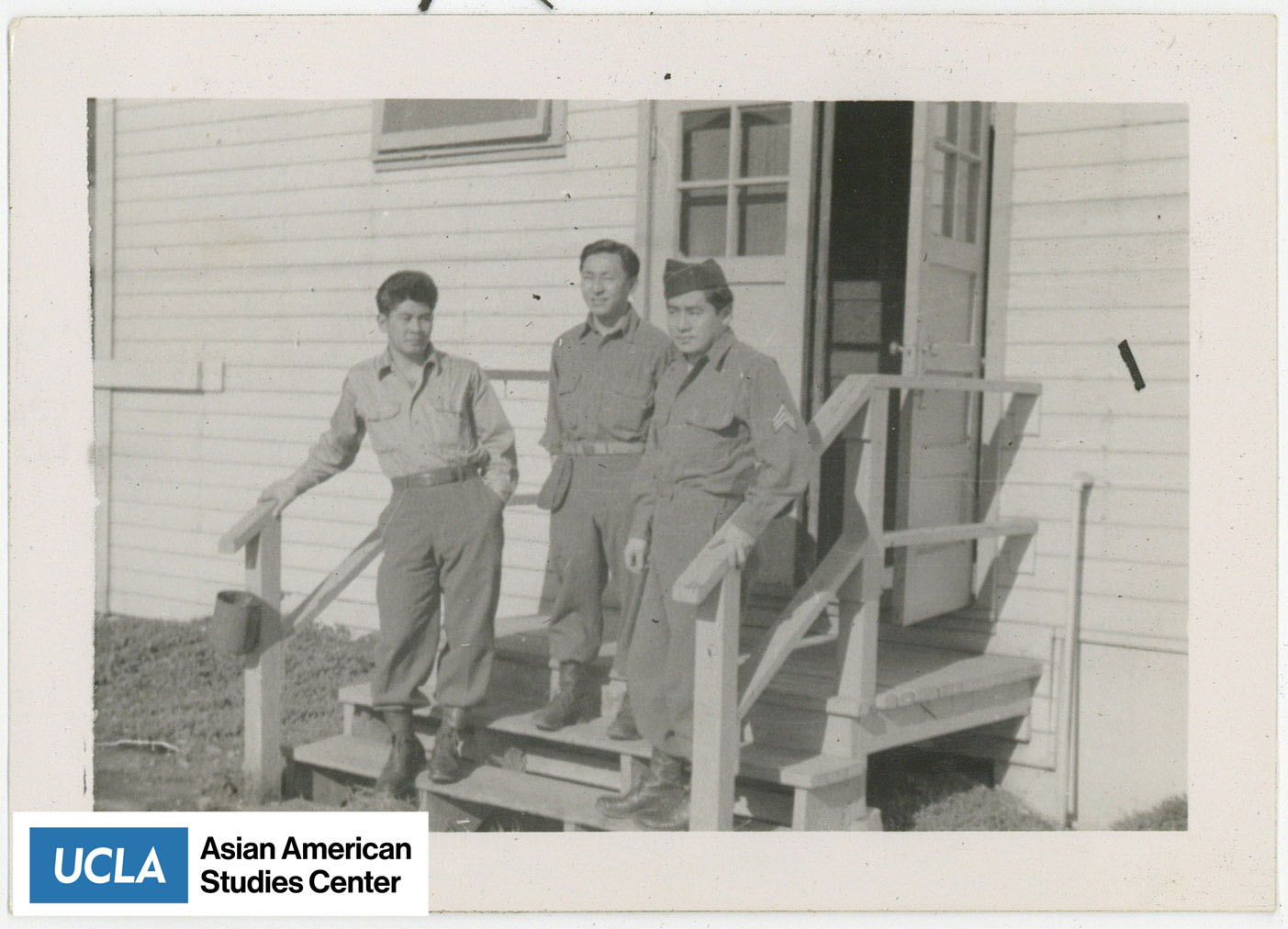 Three Nisei in military uniform stand on steps of a building.