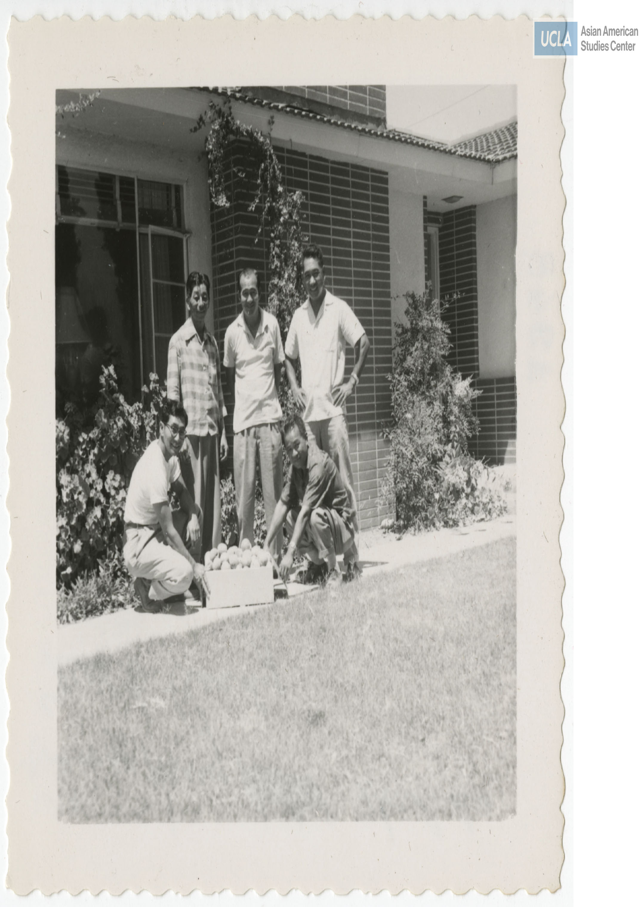 Harry Hoshiko next to Rudy Tokiwa with a box of fruits. Three men standing behind them.