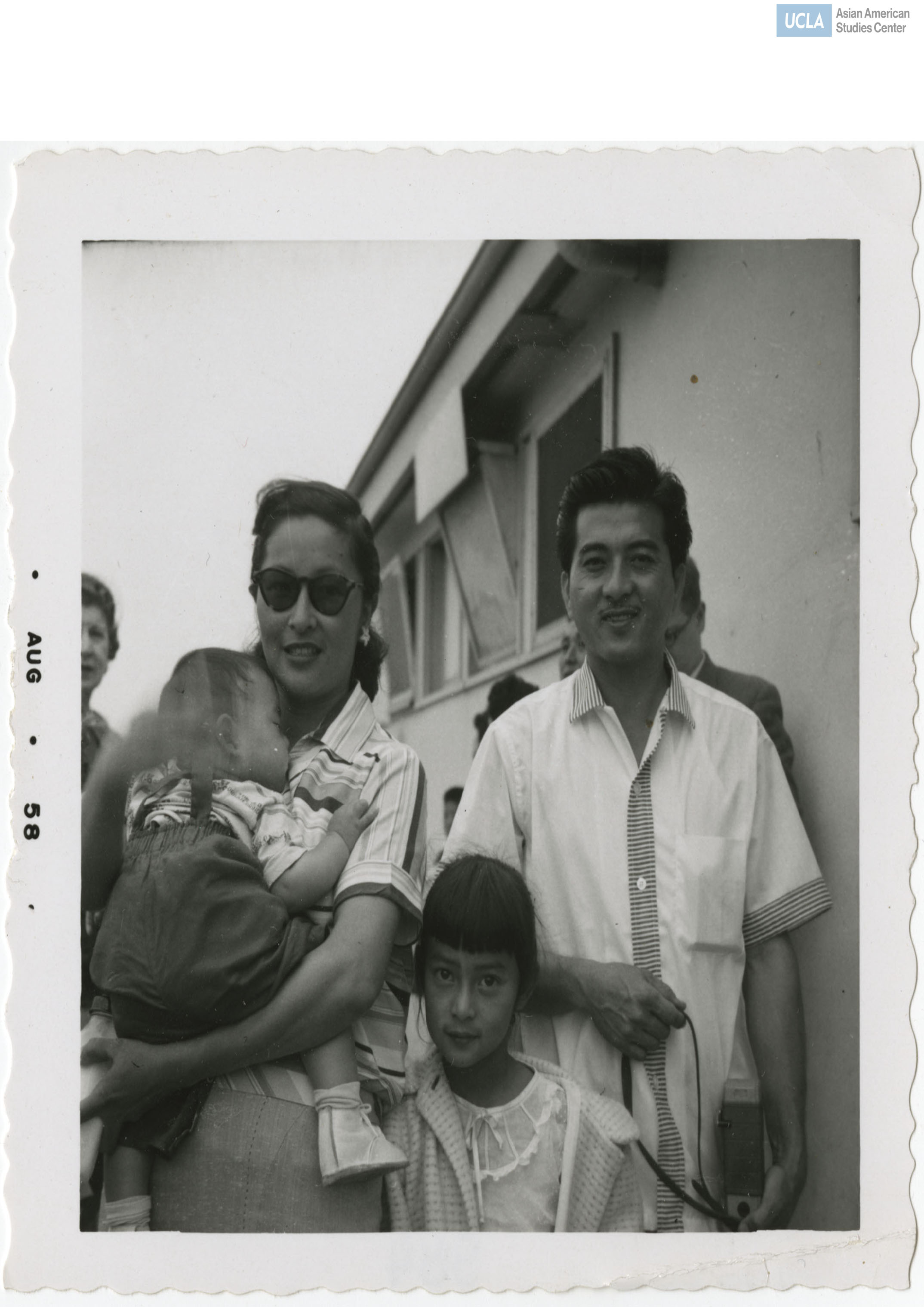 Woman is carrying a sleeping baby to the left of possibly her husband and daughter.