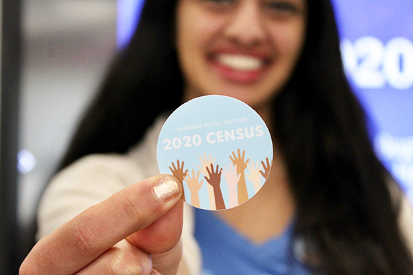 Woman holding a blue sticker that reads I pledged to fill out the 2020 Census